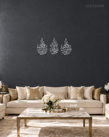 Three vertical acrylic panels in mirror silver, each with one short surah in Arabic calligraphy, hung together as a set.