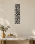 Tall vertical Kalima calligraphy in gloss piano black acrylic, stacked Thuluth lines float-mounted on a pale plaster wall above a console table