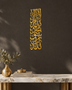 Mirror gold acrylic Kalima wall art in a tall vertical Thuluth composition, catching warm lamplight in a neutral hallway