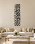 Tall vertical Kalima calligraphy in gloss piano black acrylic, stacked Thuluth lines float-mounted on a pale plaster wall above a console table