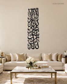 Tall vertical Kalima calligraphy in gloss piano black acrylic, stacked Thuluth lines float-mounted on a pale plaster wall above a console table