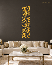 Mirror gold acrylic Kalima wall art in a tall vertical Thuluth composition, catching warm lamplight in a neutral hallway
