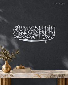 Kalima calligraphy in mirror silver acrylic, one sweeping horizontal line of Thuluth, float-mounted above a marble console