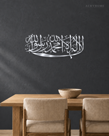 Kalima calligraphy in mirror silver acrylic, one sweeping horizontal line of Thuluth, float-mounted above a marble console