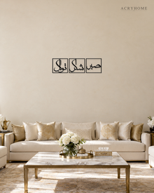 Set of three gloss black acrylic panels reading Sabr, Shukr and Tawakkul in Arabic, each inside a slim rectangular border, hung in a row on a pale ivory wall