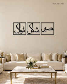 Set of three gloss black acrylic panels reading Sabr, Shukr and Tawakkul in Arabic, each inside a slim rectangular border, hung in a row on a pale ivory wall