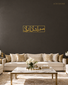 Set of three mirror gold acrylic panels reading Sabr, Shukr and Tawakkul in Arabic, each inside a slim rectangular border, hung in a row on a warm espresso wall