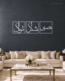 Set of three mirror silver acrylic panels reading Sabr, Shukr and Tawakkul in Arabic, each inside a slim rectangular border, hung in a row on a cool graphite wall