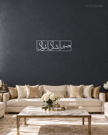 Set of three mirror silver acrylic panels reading Sabr, Shukr and Tawakkul in Arabic, each inside a slim rectangular border, hung in a row on a cool graphite wall