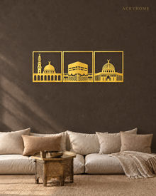 Three mirror gold acrylic panels of the holy mosques of Makkah, Madinah and Jerusalem, float-mounted side by side above a marble console.