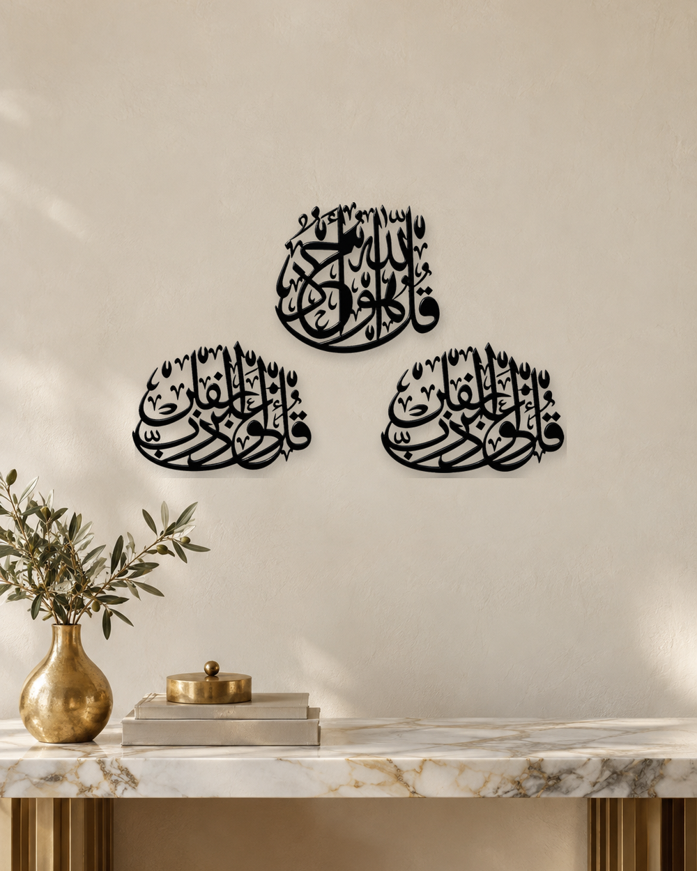 Three Quls Arabic calligraphy wall art in gloss black acrylic, one cluster above and two below, float-mounted on a pale wall.