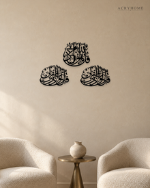 Three Quls Arabic calligraphy wall art in gloss black acrylic, one cluster above and two below, float-mounted on a pale wall.