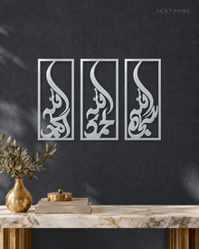 Set of three narrow vertical acrylic wall panels in mirror silver, each framing a single Arabic word in tall flowing calligraphy, float-mounted in a row on a pale wall.