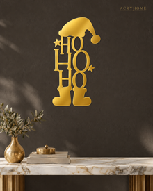 Ho Ho Ho Christmas Wall Art with Hat and Boots in mirror gold acrylic, float-mounted on a deep charcoal wall.