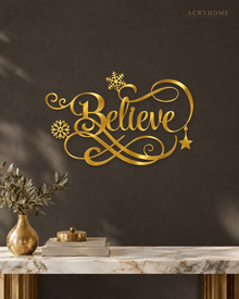 Believe in ornate flowing script with snowflake and flourish detail, laser-cut from mirror gold acrylic and float-mounted on a pale wall.