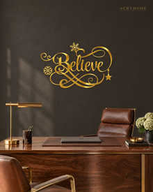 Believe in ornate flowing script with snowflake and flourish detail, laser-cut from mirror gold acrylic and float-mounted on a pale wall.
