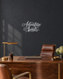 Adventure Awaits brush script wall art in mirror silver chrome acrylic, float-mounted on a light wall above a desk