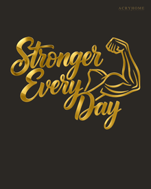 Stronger Every Day script wall art with flexed-arm icon in mirror gold acrylic, catching light on a pale gym wall.