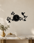 Gloss black acrylic wall clock with laser-cut branches, leaves and two small birds spreading asymmetrically either side of the dial, mounted on a pale wall.