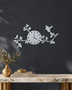Silver mirror chrome acrylic wall clock with a branch, leaf and bird design framing the dial, float-mounted on a light wall.