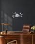 Silver mirror chrome acrylic wall clock with a branch, leaf and bird design framing the dial, float-mounted on a light wall.
