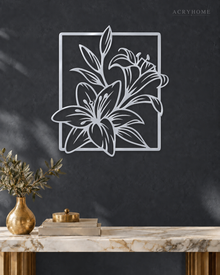 Lily line art wall piece in mirror silver acrylic, leaves reaching beyond a thin rectangular frame, float-mounted so the line lifts off the wall.