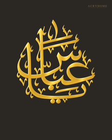 The same Arabic name calligraphy piece in mirror gold acrylic, catching warm light on a light-toned wall.