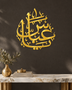 The same Arabic name calligraphy piece in mirror gold acrylic, catching warm light on a light-toned wall.