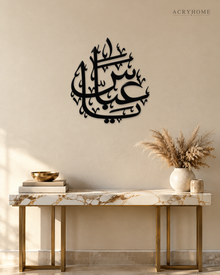 Arabic name calligraphy wall piece in gloss piano black acrylic, float-mounted above a pale console table.