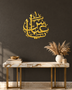 The same Arabic name calligraphy piece in mirror gold acrylic, catching warm light on a light-toned wall.