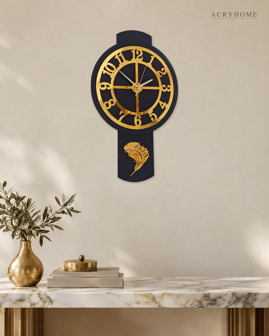 Pendulum wall clock in black and gold mirror acrylic, round dial above a long drop, on a pale wall.