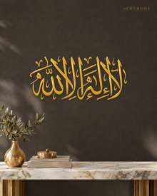 La Ilaha Illa Allah Thuluth Panel in mirror gold acrylic, float-mounted on a deep charcoal wall