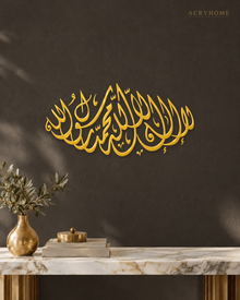 La Ilaha Illallah Shahada — Acrylic Islamic Wall Art in mirror gold acrylic, float-mounted on a deep charcoal wall